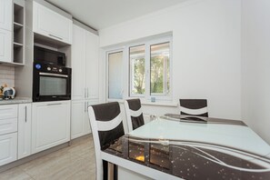 A modern kitchen with white cabinetry, a built-in oven, and a dining area with a glass table and chairs. - Studio in New Building • Elevator • Quiet Retreat (Chișinău)