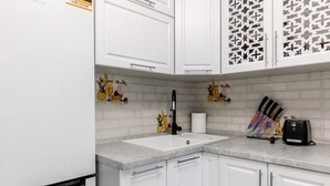 Una cocina con armarios blancos, un lavamanos, un grifo y un tostador.