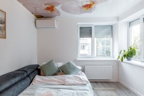 A bedroom with a bed, a radiator, a window with blinds, and a plant on the windowsill. - Studio in New Building • Elevator • Quiet Retreat (Chișinău)