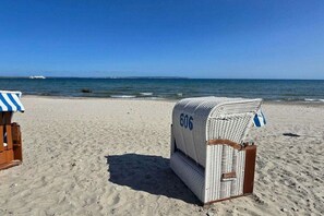 A beach with a wicker beach chair labeled '606' and a blue and white striped beach umbrella. - Stella Maris, Villa Agnes (Binz)