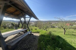 A picnic area with a bench and a shelter, overlooking a green landscape with trees and a distant view of buildings. - Holiday home in Quedlinburg with barbecue (Quedlinburg)