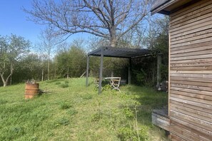 Ein Holzgebäude mit überdachter Terrasse, einer Metallbank und einem Baum.