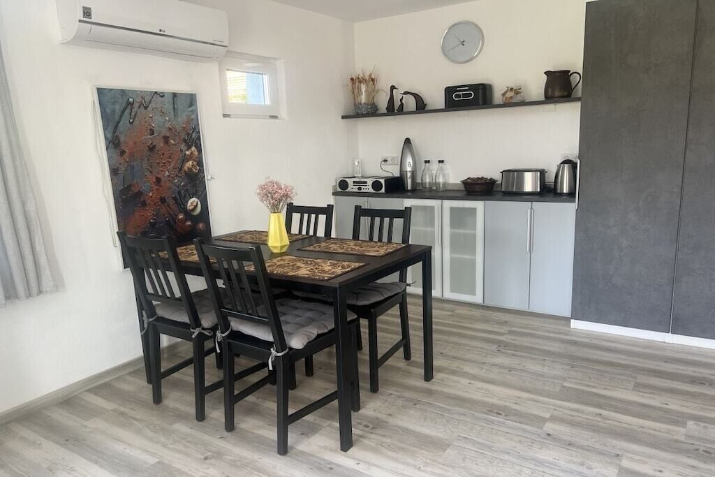 Un coin repas avec une table et des chaises, une cuisine équipée de placards et d’appareils électroménagers, et une horloge au mur.