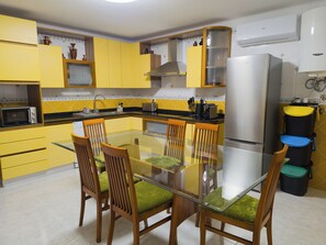 A modern kitchen with yellow cabinets, a glass dining table, and a stainless steel refrigerator. - Casa d'Avó (União das Freguesias de Felgueiras e Feirão)