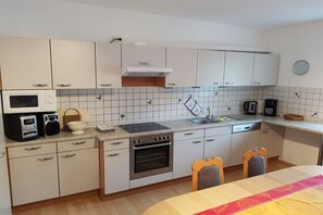 A compact kitchen with white cabinets, a microwave, an oven, a sink, and a dining area with a table and chairs. - Holiday apartment with 4 bedrooms (Fürth\/Ellenbach)