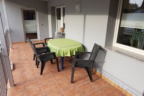 Een terras met een ronde tafel en vier stoelen, een schuifdeur en een raam met jaloezieën.
