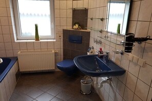 Een badkamer met een blauwe wastafel, een toilet, een radiator en een raam met een plant.