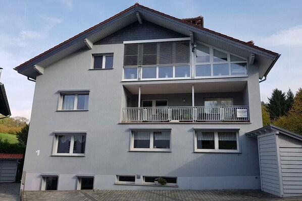 Een woonhuis met twee verdiepingen, een balkon op de bovenverdieping, een garage en een kleine tuin.