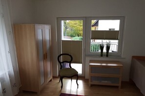 Ein Zimmer mit einem Holzschrank, einem Stuhl, einer Bank und einem Fenster mit Jalousien.