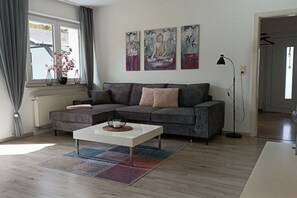Un saló modern amb un sofà gris, una taula de cafè blanca i obra d'art a la paret.