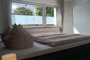 A bedroom with a bed, pillows, a window with curtains, and a radiator. - Holiday apartment with 1 bedroom (Schmallenberg-Grafschaft)