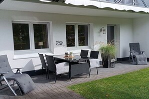 Een terras buiten met een tafel, stoelen, een bloempot en een bordje met de tekst 'Welcome to Garden'.