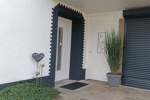 Entrada d'un edifici amb una porta blanca, una porta amb marc negre, una planta en test i una placa amb forma de cor.