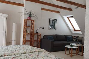 A room with a bed, a sofa, a small table, a bookshelf, a potted plant, and a skylight. - Holiday apartment Gries"scher Hof (Satjendorf)