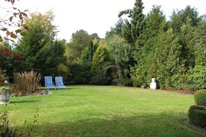 A well-maintained garden with a lawn, two striped chairs, and a variety of trees and shrubs. - Heideblockhaus-Erika (Neuenkirchen)