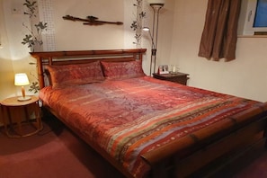 A bedroom with a wooden bed, a bedside lamp, and a nightstand. - Heideblockhaus-Erika (Neuenkirchen)