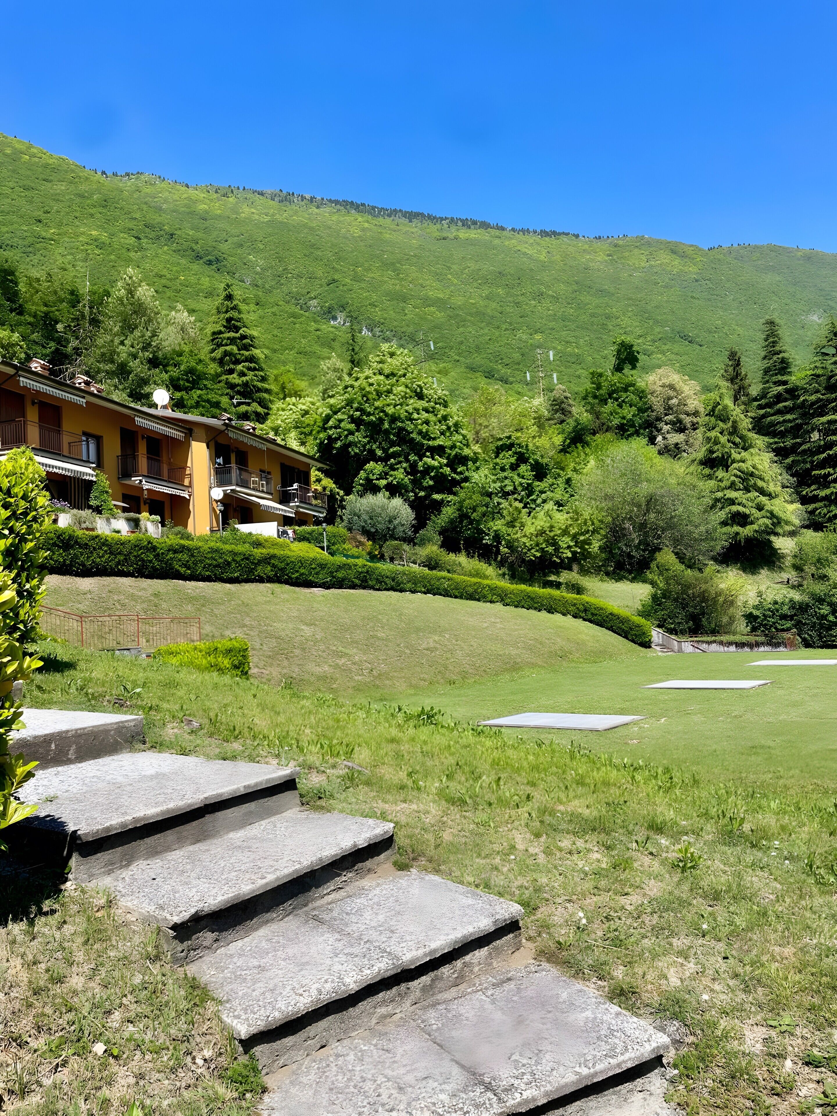Un hôtel doté d’un escalier en pierre menant à un espace verdoyant, entouré d’une végétation luxuriante et avec une chaîne de montagnes en toile de fond.