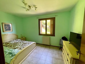 A bedroom with a bed, a dresser, a radiator, a window, and a ceiling fan.