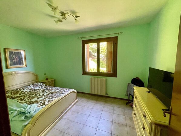 Une chambre à coucher avec un lit, une commode, un radiateur, une fenêtre et un ventilateur de plafond.