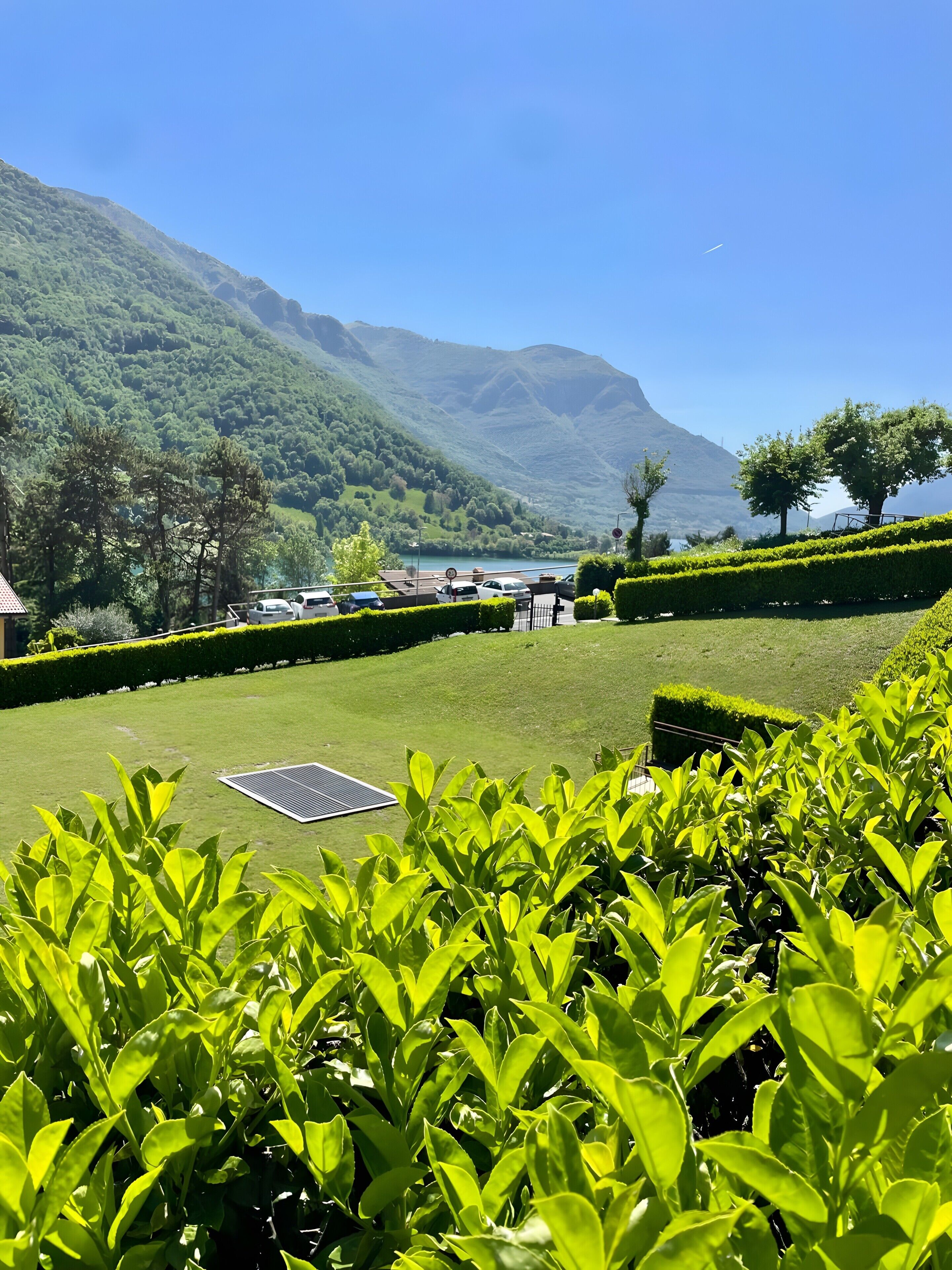 Un jardin bien entretenu, équipé d’un panneau solaire, avec un espace de stationnement pour voitures et une vue sur un lac et des montagnes en arrière-plan.