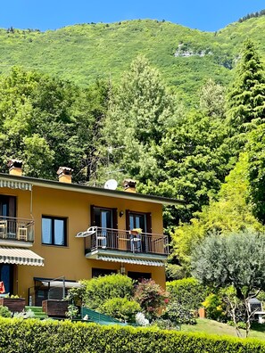 Un bâtiment jaune doté d’un balcon, entouré d’une végétation luxuriante et de collines.