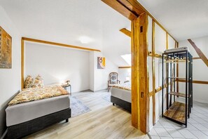 A room with two beds, a wooden beam structure, a chair, and a metal shelf unit. - Holiday home with 1 bedroom (Königsee \/ OT Barigau)