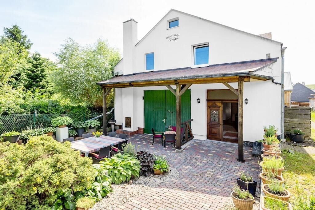 Un bâtiment blanc doté d’un patio couvert, d’une porte verte et d’un espace extérieur aménagé pour s’asseoir.