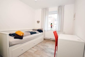 Une chambre à coucher avec un lit, un bureau, une chaise et une fenêtre avec des rideaux.