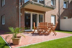 A brick building with a patio area featuring a wooden table and chairs, a potted plant, and a sliding glass door. - Holiday apartment with 2 bedrooms (Norden-Norddeich)