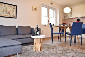Un salon moderne avec un canapé gris, une table basse ronde en bois et un coin repas comprenant des chaises bleues et une table blanche.