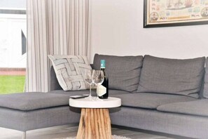 A modern living room with a grey sofa, a round wooden coffee table, a wine bottle, and a glass on the table. - Holiday apartment with 2 bedrooms (Norden-Norddeich)