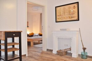 A room with a bed, a white fireplace, a framed ship illustration, and a small table. - Holiday apartment with 2 bedrooms (Norden-Norddeich)