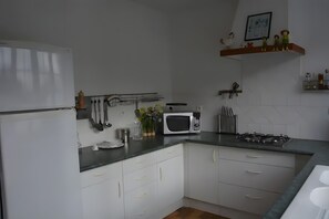 Een keuken met witte kastjes, een magnetron, een gasfornuis en diverse keukengerei aan de muur.