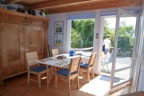 A room with a wooden cabinet, a table with chairs, and a sliding glass door leading to an outdoor area. - Holiday apartment with 1 bedroom (Fehmarn)