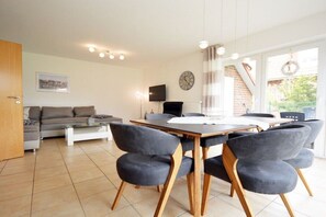 Een moderne woonkamer met een bank, een eettafel met stoelen, een televisie en een klok aan de muur.