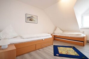 Een knus kamertje met twee bedden, een nachtkastje, een lamp en een lijst met een afbeelding aan de muur.
