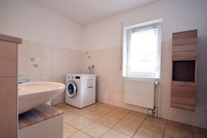 Een kleine badkamer met een wastafel, een wasmachine en een raam voor natuurlijk licht.