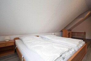 A single bed in a room with a sloped ceiling, a nightstand with a lamp, and a wooden headboard. - Holiday home with 2 bedrooms (Norddeich)
