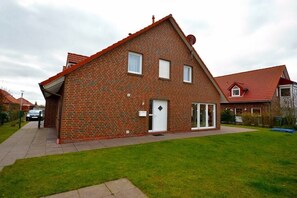 Een twee verdiepingen tellend huis van baksteen met een rood dak, een voordeur en een kleine voortuin.