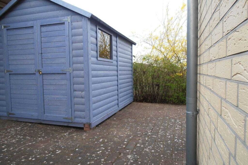 Un cobertizo de madera azul con una ventana y una puerta, junto a un muro de ladrillo.