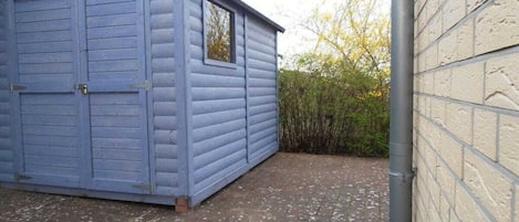A blue wooden shed with a window and a door, adjacent to a brick wall.