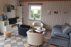 A living room with a sofa, armchairs, a television, and a window with a view of greenery. - Holiday home with 1 bedroom (Waren (Müritz))
