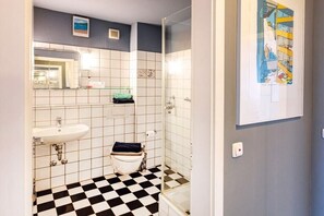 Kylpyhuone, jossa on ruutukuviollinen lattia, pesuallas, wc ja suihku.