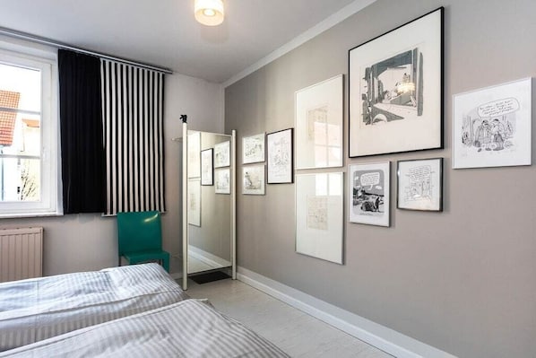 A bedroom with a bed, a mirror, and a wall with framed pictures. - Cartoon in Karoline's House (Binz)