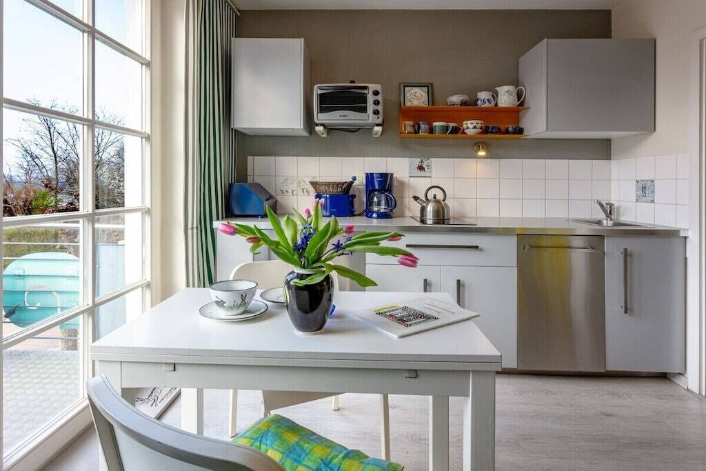 Eine moderne Küche mit weißer Arbeitsplatte, einem Wasserkocher, einer Kaffeemaschine und einem Toaster. Ein Fenster bietet einen Blick nach draußen.