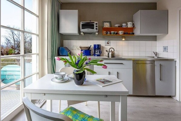 Eine moderne Küche mit weißer Arbeitsplatte, einem Wasserkocher, einer Kaffeemaschine und einem Toaster. Ein Fenster bietet einen Blick nach draußen.