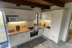 A modern kitchen with white cabinets, a microwave, a coffee maker, and a tiled backsplash. - Holiday home with 1 bedroom (Friedrichskoog)