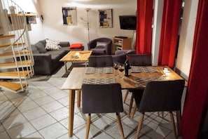 A dining area with a wooden table and chairs, a sofa, a TV, and a staircase. - Holiday home with 1 bedroom (Friedrichskoog)