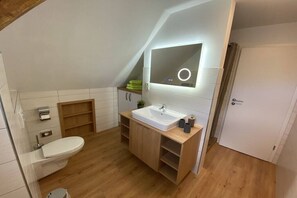 Een moderne badkamer met een wit wastafel, houten opbergmeubel en een spiegel met verlichting.