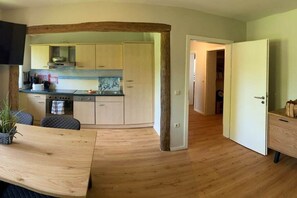 Una cocina moderna con armarios de madera clara, horno empotrado y comedor con mesa y sillas de madera.
